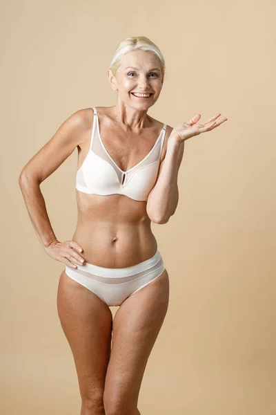 Studio shot of beautiful mature woman with blonde hair in white underwear  posing for camera, standing isolated over beige background Stock Photo by  ©kostiantynvoitenko 468421126