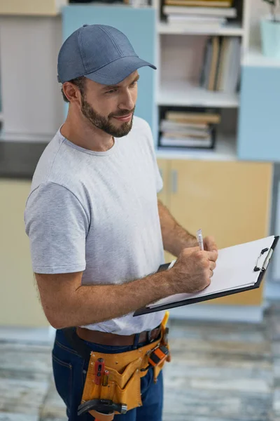 Quality service. Professional young repairman making notes on clipboard while standing indoors