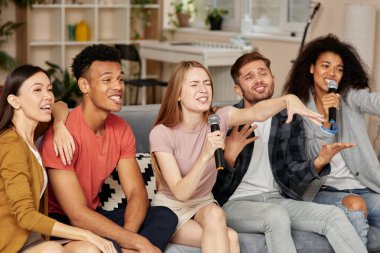 Karaoke zamanı. Evde karaoke yapan, mikrofonla şarkı söyleyen, oturma odasındaki kanepede otururken birlikte harika vakit geçiren bir grup neşeli genç çok kültürlü arkadaş. Karaoke partisi