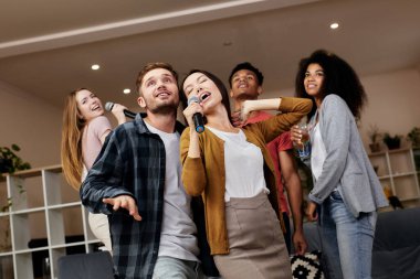 Parti zamanı. Neşeli genç arkadaşlar mikrofon tutuyorlar ve evde arkadaşlarıyla karaoke yaparken birlikte şarkı söylüyorlar. Bir grup insan evde eğleniyor.