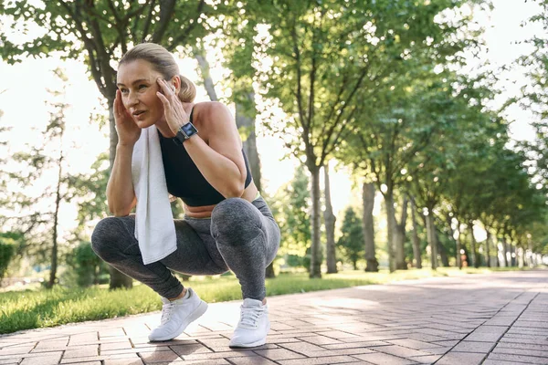 Zrób to dla siebie. Zmęczony w średnim wieku atletyczna kobieta w odzieży sportowej odwraca wzrok, odpoczywając podczas treningu w zielonym parku w słoneczny dzień — Zdjęcie stockowe