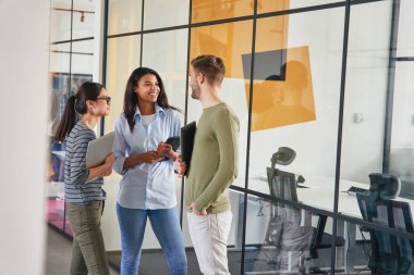 Üç iş arkadaşı koridorda sohbet ediyor.