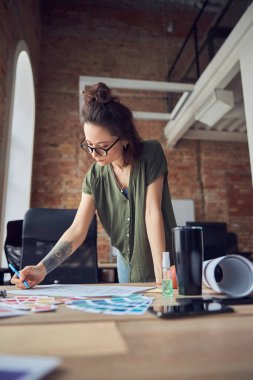 Yaratıcı kadın, iç mimar, gözlük takan, kalemle notlar alan, yeni bir proje üzerinde çalışan, ofisinde duran.