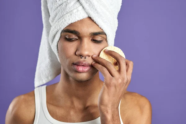 Retrato de cerca de un joven guapo limpiando la piel con almohadillas de algodón sobre un fondo púrpura aislado — Foto de Stock