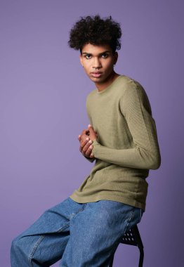 Genç transseksüel adam stüdyoda oturuyor. Siyah kıvırcık saçlı, seksi erkek.