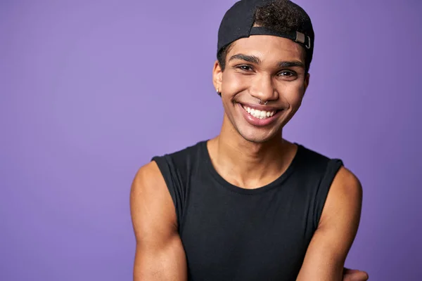 Ritratto di uomo transgender latino sorridente in t-shirt nera e cappuccio su sfondo viola — Foto Stock