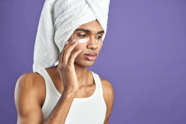 Primer plano retrato de joven latinoamericano hombre en toalla aplicar bajo parches de colágeno en los ojos — Foto de Stock