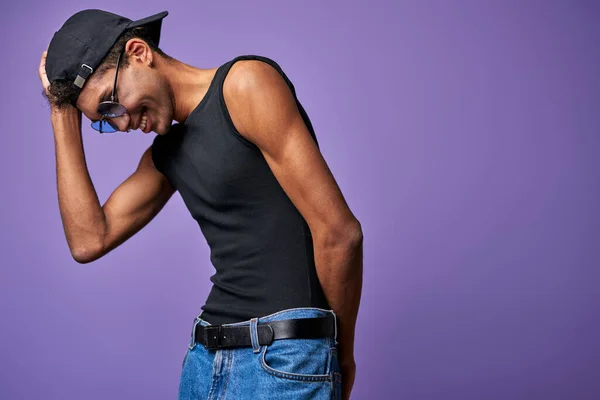 Uomo latino sorridente in t-shirt nera e cappello in posa su sfondo viola ritratto. Giovane transgender — Foto Stock