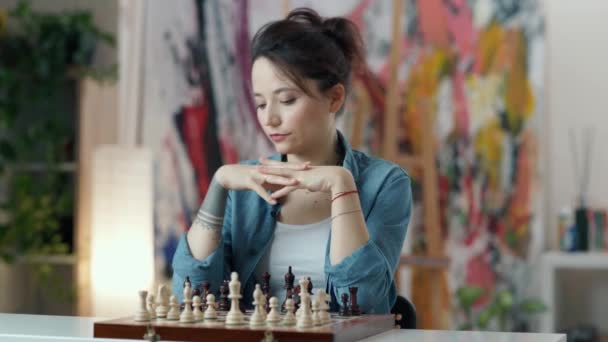 Gyakorold az agyad. Fiatal nő gondolkodik sakk lépés, miközben otthon ül, és sakkozik egyedül — Stock videók