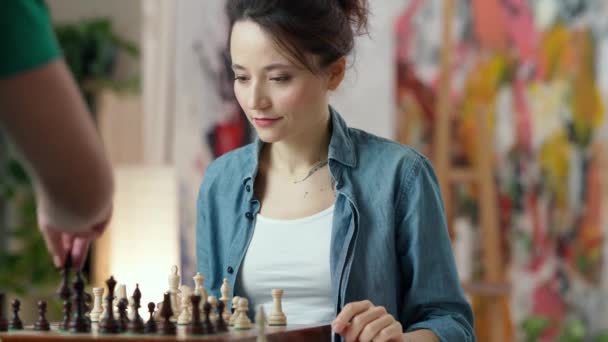 체스 말을 보고 있는 젊은 여자는 집에서 남자 친구와 체스를 두는 동안 체스를 두고 이길 생각을 하고 있습니다 — 비디오