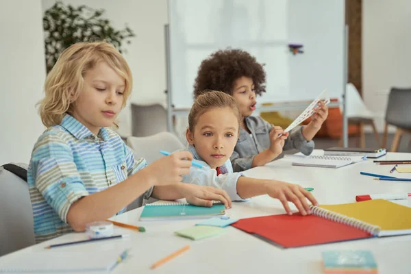 Actividad social. Niños diversos sentados juntos en la mesa en el aula de la escuela primaria — Foto de Stock