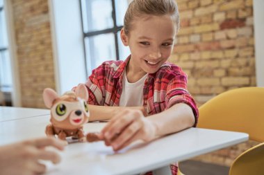 Çekici küçük kız masada oturuyor, teknik oyuncakları inceliyor ve gülümsüyor, mühendislik kulübünde vakit geçiriyor.