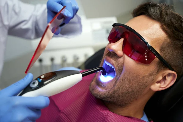 Diş muayenesindeki genç adam mavi ışıkla tedavi görüyor.