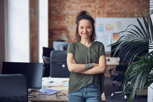 Portrait of happy woman, interior designer or architect smiling at camera while standing with arms crossed in modern green office on a daytime