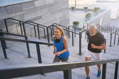 Şehirde merdivenlerden koşarak çıkan bir çift, dışarıda birlikte egzersiz yapıyorlar. Aktif spor, fitness, orta yaşlı insanların sağlıklı yaşam tarzı