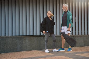 Sportif orta yaşlı erkek ve kadın spor giyim kuşamında neşeli görünüyor, sohbet ederken birlikte dışarıda antremana hazırlanıyorlar.