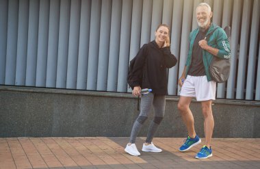 Neşeli orta yaşlı sporcular, spor kıyafetli kadın ve erkek kameraya gülümsüyor, birlikte dışarıda antrenmana hazırlanıyorlar.