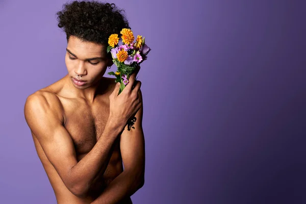 Érzéki transznemű férfi lila hátterű csokorral. Sportos sportoló virágokkal a kezében — Stock Fotó