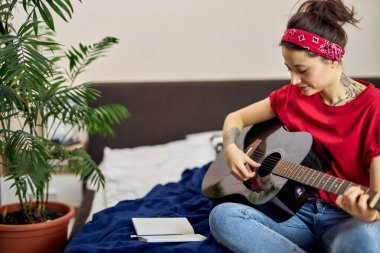 Evde bir yatakta oturmuş gitar çalan hoş bir genç kadın.