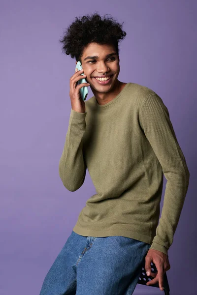 Porträt eines jungen brünetten Mannes, der Handy in der Hand auf lila Hintergrund sitzt — Stockfoto