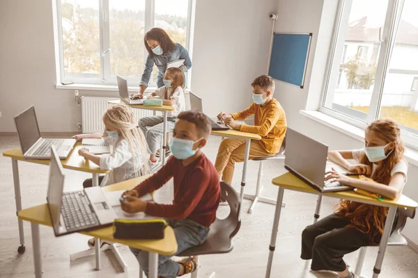 Niños con máscaras sentados en sus escritorios en clase — Foto de Stock