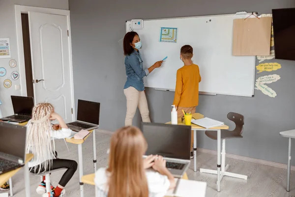 Nauczyciel w masce stojący przy tablicy i uczący chłopiec — Zdjęcie stockowe