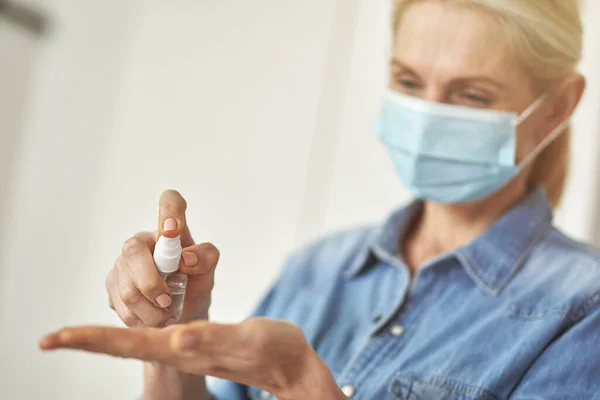 Närbild skott av kvinna i skyddande ansiktsmask rengöring händerna med antibakteriell hand saneringsmedel gel pump — Stockfoto
