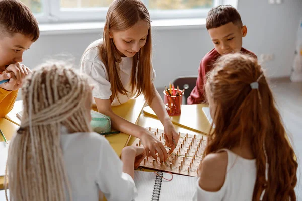 Crianças em idade escolar sorrindo usando geoboard em sala de aula juntas — Fotografia de Stock