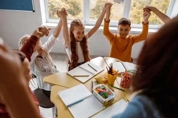 Niños sentados en la mesa y levantando las manos — Foto de Stock