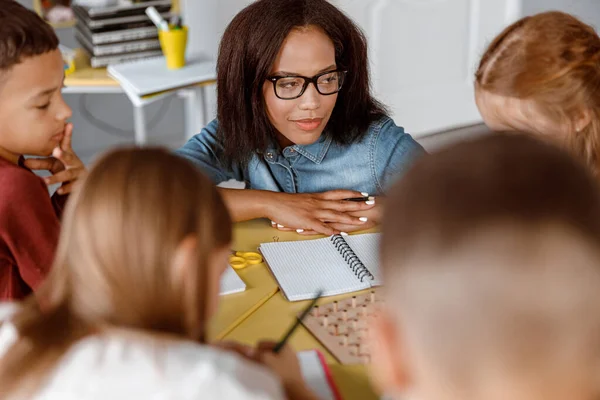 Ders sırasında gözlüklü öğretmen okul çocuklarına bakıyor.