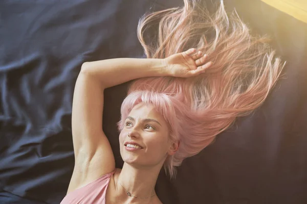 Gedachte vrouw met stijlvol roze haar rust op groot comfortabel bed — Stockfoto