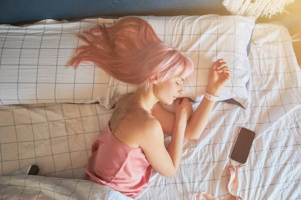 Kobieta z różowymi włosami i dużym tatuażem na plecach śpi w wygodnym łóżku — Zdjęcie stockowe