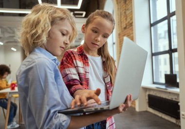 İki meraklı çocuk, küçük çocuk ve kız BTMM dersi sırasında sınıfta dikilirken dizüstü bilgisayar kullanıyorlar.