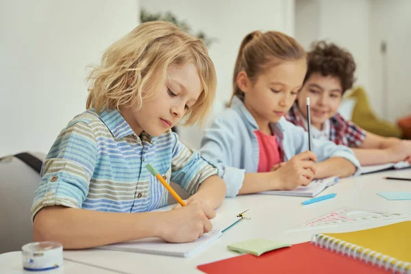 Kvalitetsutbildning. En flitig skolpojke gör anteckningar under lektionen. Barn som studerar, sitter tillsammans vid bordet i grundskolans klassrum — Stockfoto