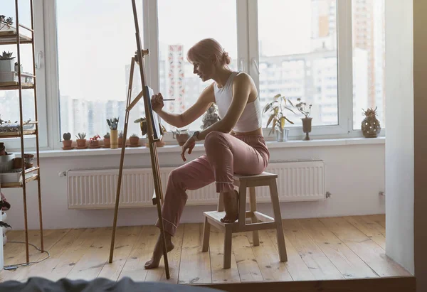 긍정적 인 젊은 여성 미술가가 드넓은 발코니에 있는 이젤에서 일한다 — 스톡 사진