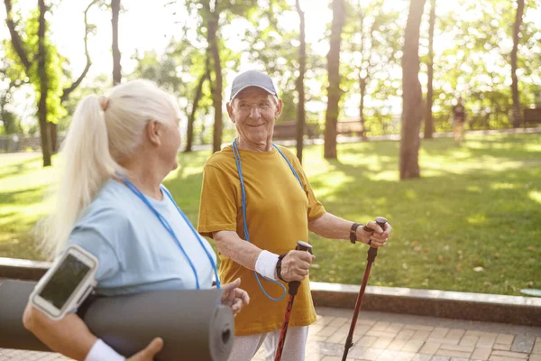 Lächelnder Senior mit Stöcken für Nordic Walking und Frau im grünen Park — Stockfoto