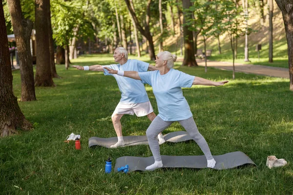 Mujer madura feliz con pareja hacer ejercicios de yoga en el césped exuberante —  Fotos de Stock