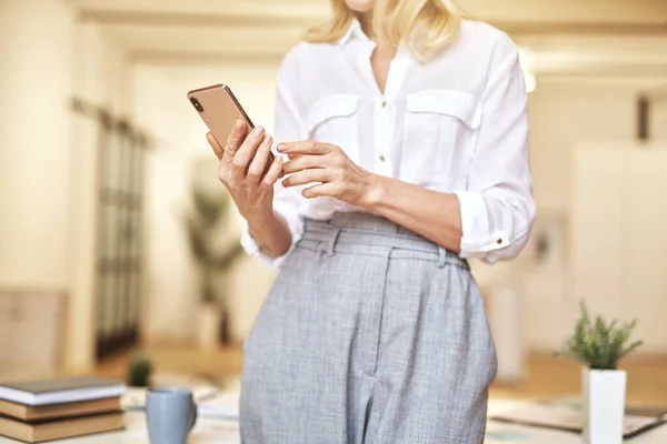 Foto yang dipotong dari wanita pengusaha dewasa bergaya memegang dan menggunakan smartphone-nya saat berdiri di kantor modern — Stok Foto