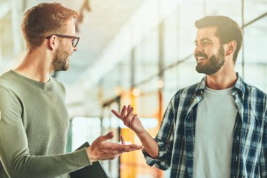 İki genç erkek öğrenci koridorda bir şey tartışıyor.