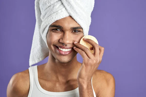 Retrato de hombre guapo limpiando la cara y mirando la cámara con almohadillas cosméticas sobre fondo púrpura — Foto de Stock