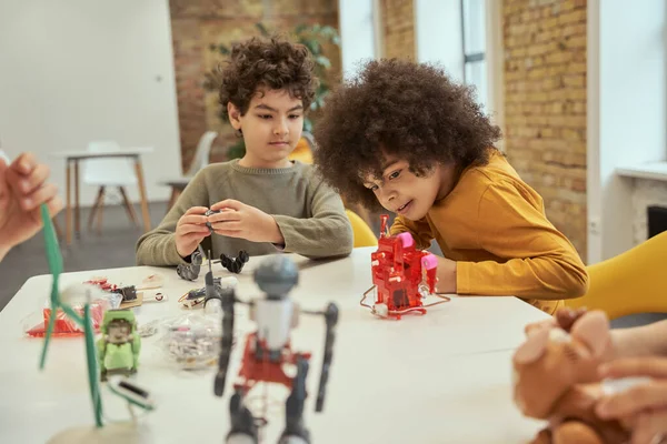 Enthusiastic little boy with afro hair smiling while putting an electronic toy kit together, spending time with friends at engineering club — Stock Photo, Image