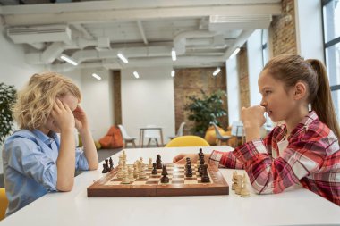 Kararlılık. Yoğunlaşmış erkek ve kız, satranç oynarken birbirlerine bakıyorlar, okulda masada birlikte oturuyorlar.