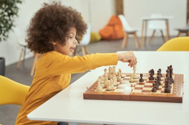 Senin sıran. Akıllı küçük çocuk satranç oynarken mutlu görünüyor, masada oturuyor.