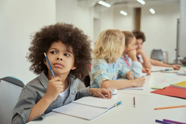 Niño curioso mirando hacia otro lado durante la lección. Niños estudiando y tomando notas, sentados juntos en la mesa de la escuela primaria — Foto de Stock