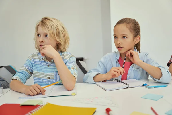 Pequeño escolar atento y colegiala estudiar y escuchar al maestro, sentados juntos en la mesa en el aula de la escuela primaria — Foto de Stock