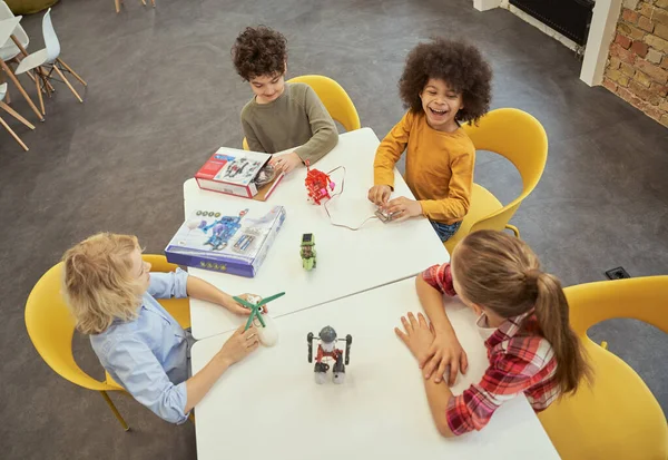 Intressanta lektioner. Hög vinkel syn på glada olika barn sitter vid bordet, undersöka tekniska leksaker fulla av detaljer, spendera tid på ingenjörsklubben — Stockfoto