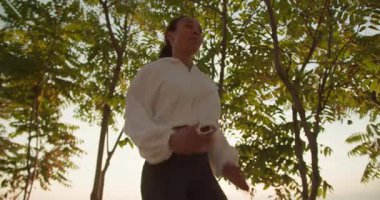 Bir kadın açık havada koşuyor, uzun ağaçlarla çevrili, renkli bir güneşin nefes kesen güzelliği sırasında.