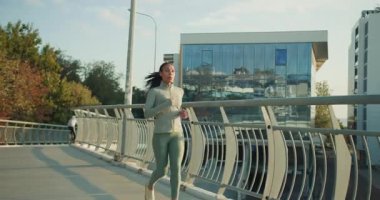 Bir kadın, temiz hava ve zindelikten zevk alarak güzel ve manzaralı bir şehir yolunda enerjik bir şekilde koşar.