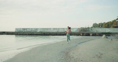 Bir kadın sakin bir plajda zarif bir şekilde koşar. Huzurlu ve huzurlu bir ortamda zindeliğini ve sağlığını gösterir.