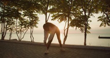 Huzurlu ve huzurlu bir günbatımı sahnesi sahnesinde bir kadın plajda egzersizlerini nazikçe yapıyor.